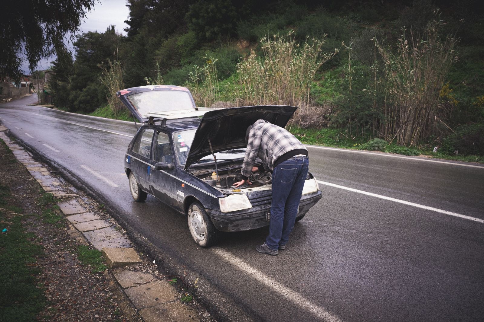 A mechanic repairing a car on the side of a rainy road